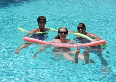 3 ladies on pool noodles in the water smiling at camera.