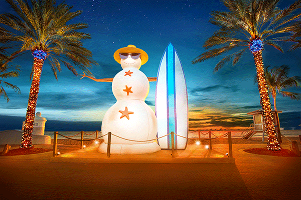 Lighting display of a snowman with a surfboard, on the beach.
